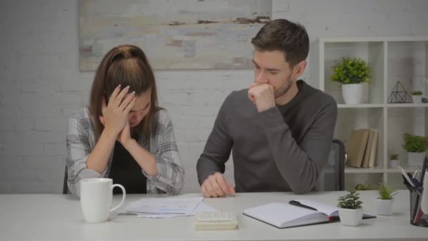Mann beruhigt aufgebrachte Frau, die mit Tabellen und Tasse am Schreibtisch sitzt  - Filmmaterial, Video