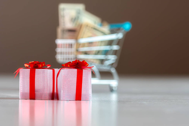 Karácsonyi kiadástervezés koncepció, ajándékdobozok bevásárlókosárral tele pénzzel homályos háttérrel - Fotó, kép