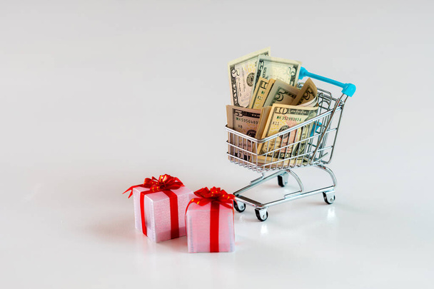 Christmas expense planning concept , gift boxes and shopping cart full of money, isolated on white - 写真・画像