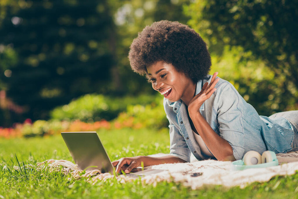 Side profile photo of black skinned young female student lying on grass working with computer web conversation joking laughing - Fotografie, Obrázek