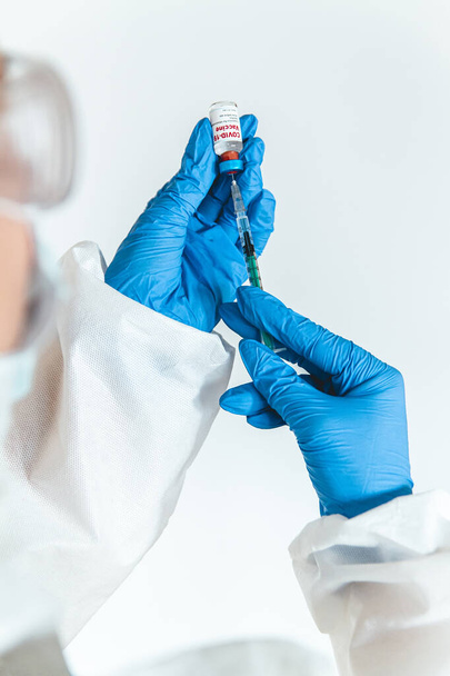 Doctor or nurse in a protective suit holds a syringe and a covid 19 vaccine - Foto, Bild