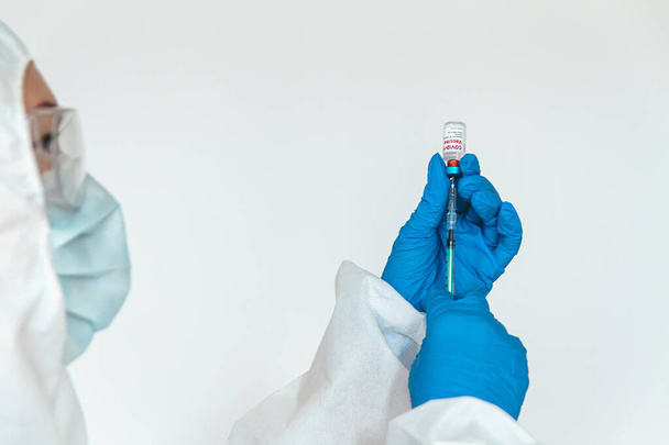 Lékař nebo zdravotní sestra v ochranném obleku drží injekční stříkačku a kovid 19 vakcínu - Fotografie, Obrázek