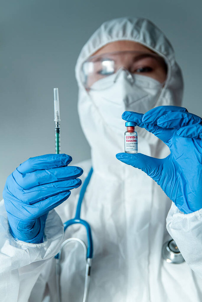 Doctor or nurse in a protective suit holds a syringe and a covid 19 vaccine - Zdjęcie, obraz