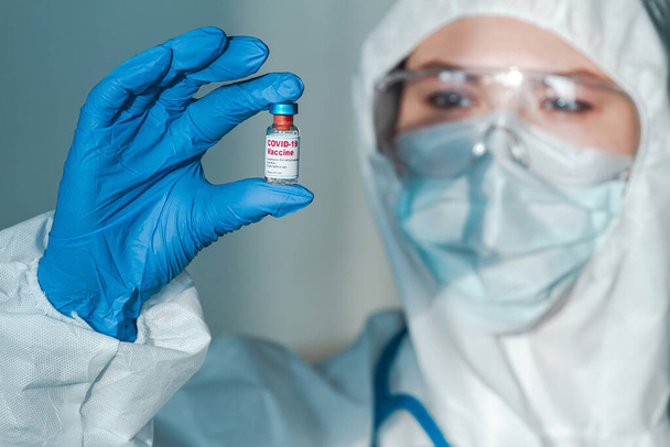 Doctor or nurse in a protective suit holding the covid 19 vaccine in hand - Foto, afbeelding