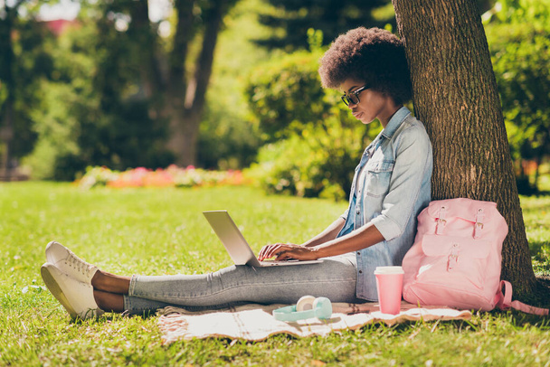 Full length body size side profile photo of black skinned woman with curly hair working on laptop browsing internet in city park - Photo, Image