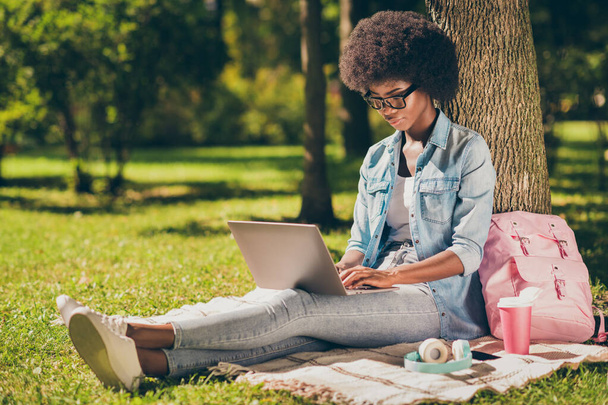 Full length body size photo of black skinned female student working on laptop learning outside green city park wearing casual denim outfit - Фото, изображение