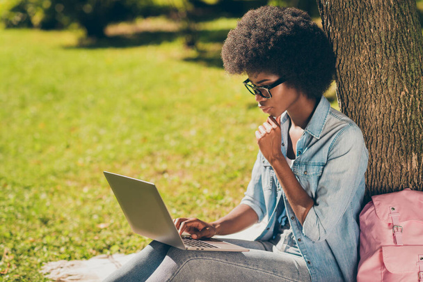 Side profile photo of black skinned serious girl using laptop touching chin learning outside the city park wearing eyewear - Foto, immagini