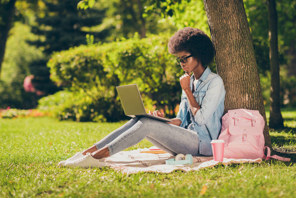 Full length body side profile photo of black skinned serious girl reading on laptop touching chin outside the city park wearing spectacles - Valokuva, kuva