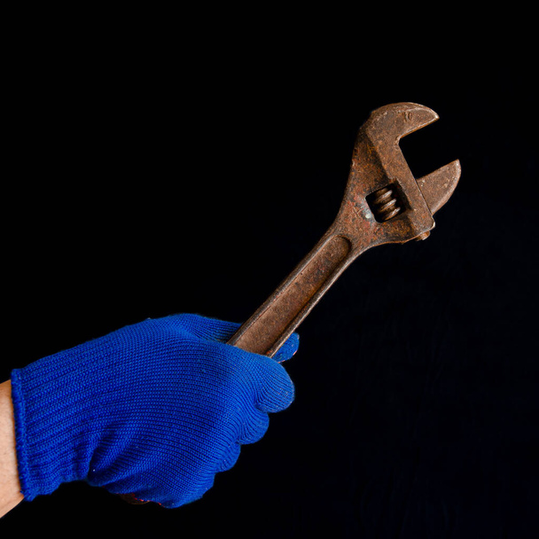 Die Hand eines Mannes in einem blauen Handschuh hält einen rostigen Schraubenschlüssel - Foto, Bild