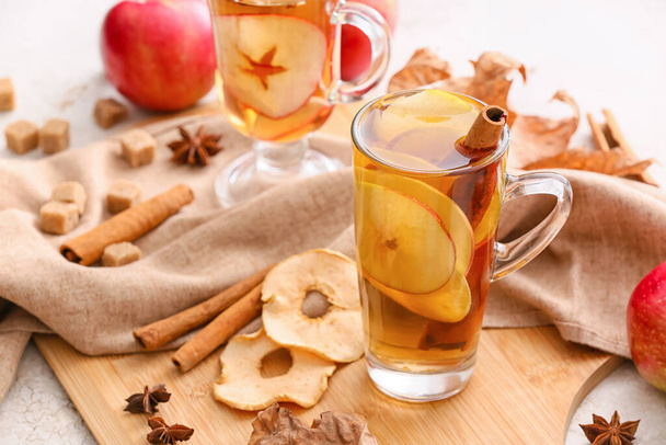 Tasty drink with spices and apple slices in cup on light table - Photo, Image