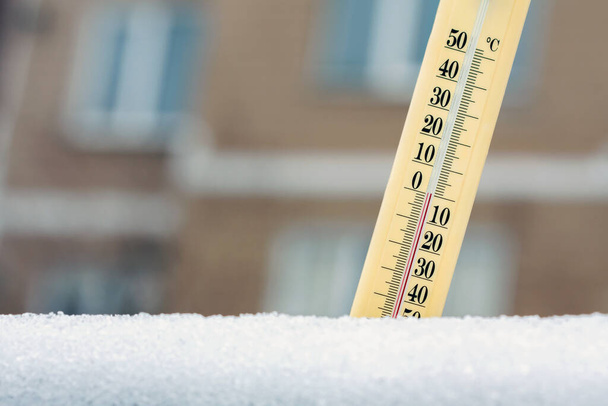Zimą. Termometr w śniegu pokazuje temperaturę około zera na tle wielopiętrowego budynku. Koncepcja prognozy pogody. - Zdjęcie, obraz