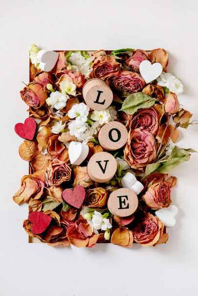 Beautiful botanical composition for st. Valentines Day. Creative layout with dry roses, petals, white flowers, small hearts and LOVE letters in white paper frame. Flat lay, close up - Fotoğraf, Görsel