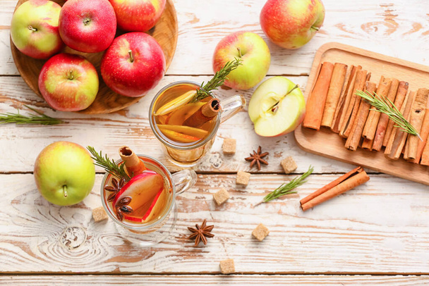 Lekker drankje met specerijen en appelschijfjes in kopjes op houten ondergrond - Foto, afbeelding