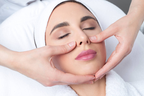 jonge vrouw doet facial massage in een schoonheidssalon. - Foto, afbeelding