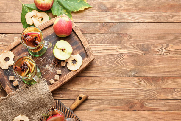 Tasty drink with spices and apple slices in cups on wooden background - Foto, afbeelding