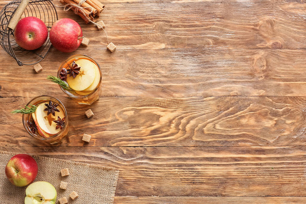 Boisson savoureuse avec des épices et des tranches de pomme dans des verres sur fond de bois - Photo, image