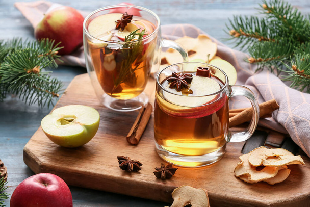 Smaczny napój z przyprawami i plasterkami jabłek w kubkach na kolorowym drewnianym tle - Zdjęcie, obraz