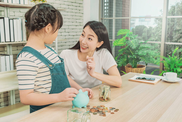 Asiatische Mutter lehrt ihre Tochter über finanzielles Sparen und Geldmanagement mit Sparschwein und Spardose. - Foto, Bild
