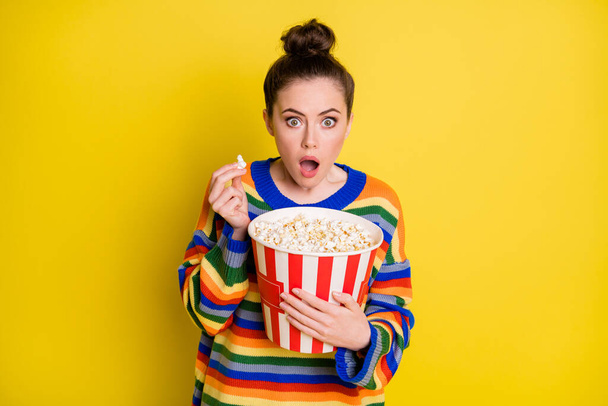 Photo of young woman amazed surprised shocked eat pop-corn watch thriller movie isolated over yellow color background - 写真・画像