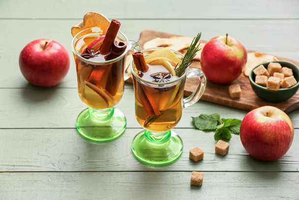 Tasty drink with spices and apple slices in cups on color wooden background - Photo, Image