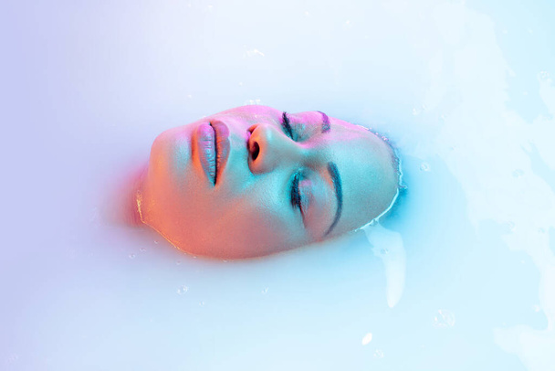 close-up vrouwelijk gezicht in de melk bad met zacht gloeien in neon licht - Foto, afbeelding