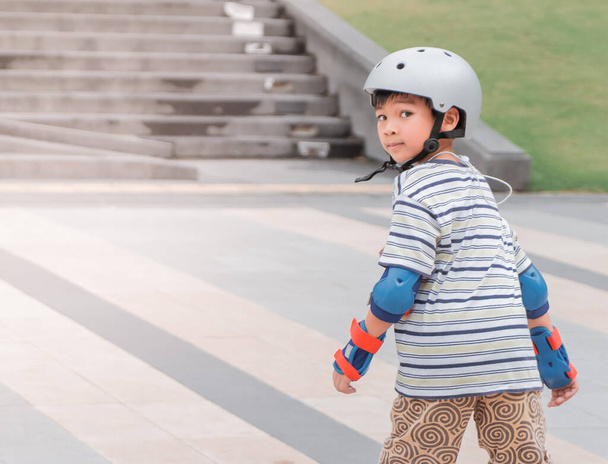 Little Asian Boy is learning to Skate on an Rollerblade in park with full protection gear and helmet. - Photo, Image