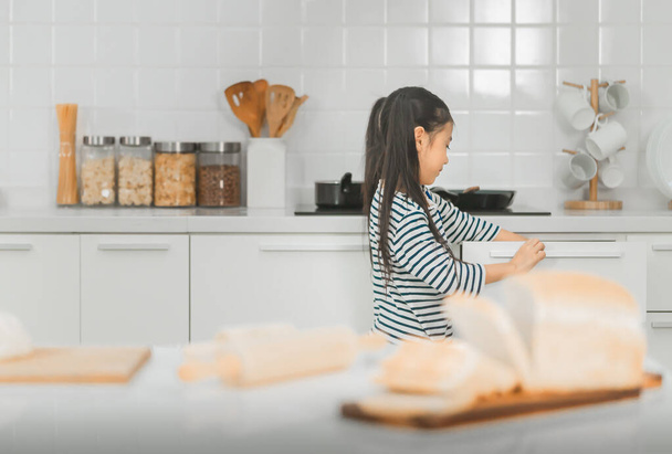 Petite fille est à la recherche de nourriture et de couverts dans la cuisine de la maison pour préparer son propre petit déjeuner. - Photo, image