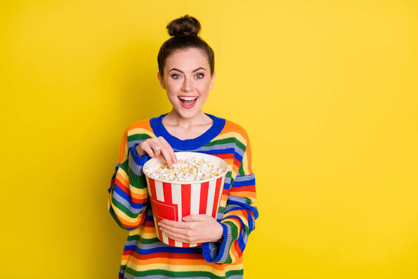 Photo of young attractive woman happy smile hold pop-corn box eat watch movie isolated over yellow color background - Photo, Image