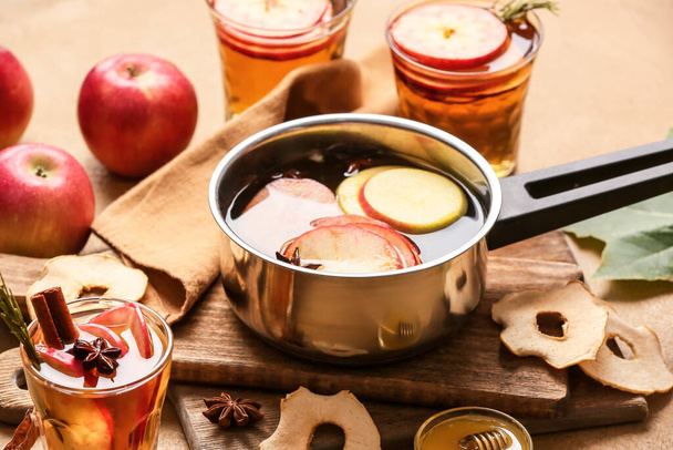Ízletes ital fűszerekkel és almaszeletekkel főzőedényben és poharakban színes háttérrel - Fotó, kép