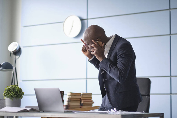 frustrated African American businessman talking on phone annoyed stressed boss manager make call arguing by mobile telephone sit at office desk - Photo, Image