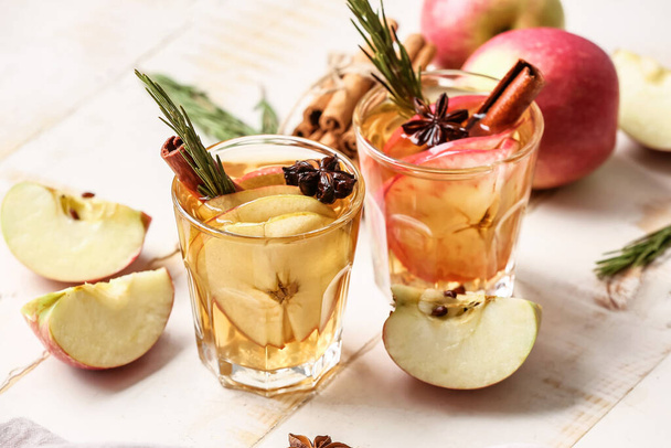 Sabrosa bebida con especias y rodajas de manzana en vasos sobre fondo de madera clara - Foto, imagen