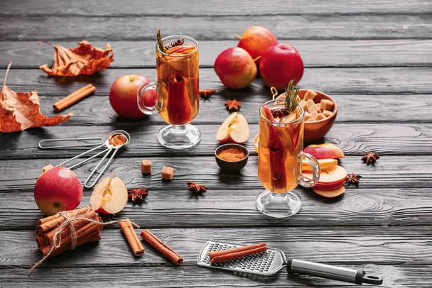 Leckeres Getränk mit Gewürzen und Apfelscheiben in Tassen auf dunklem Holzhintergrund - Foto, Bild