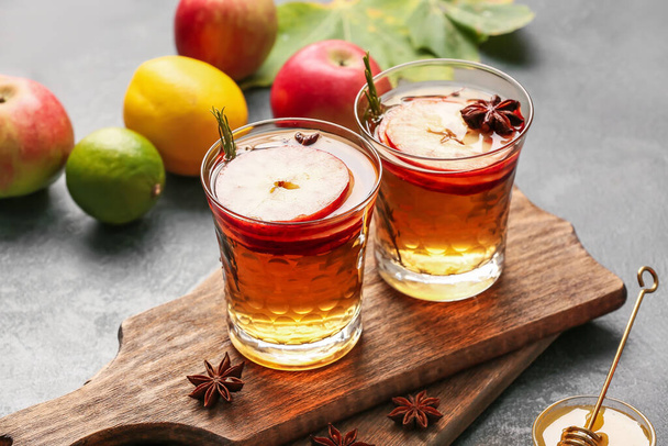 Lekker drankje met specerijen en appelschijfjes in glazen op donkere achtergrond - Foto, afbeelding