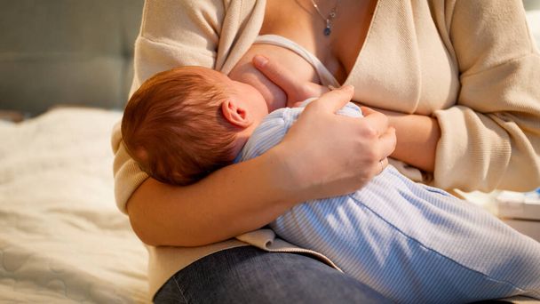Słodkie noworodki wysysające mleko z piersi matki, siedzące w nocy. Pojęcie zdrowego i naturalnego odżywiania dzieci. Zdrowie matki i dziecka. - Zdjęcie, obraz