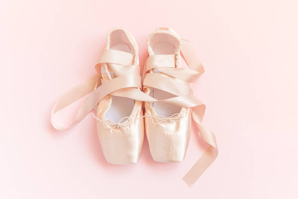 Nové pastelové béžové baletní boty se saténovou stuhou izolované na růžovém pozadí. Ballerina klasické špičaté boty pro taneční trénink. Koncept baletní školy. Horní pohled plochý prostor pro kopii - Fotografie, Obrázek
