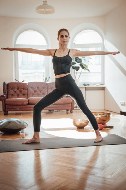 Fröhliche Frau in Sportkleidung macht Yoga auf Teppich im Zimmer - Foto, Bild
