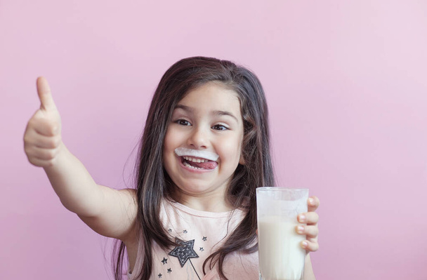 Маленькая улыбающаяся девочка пьет молоко из стакана - Фото, изображение