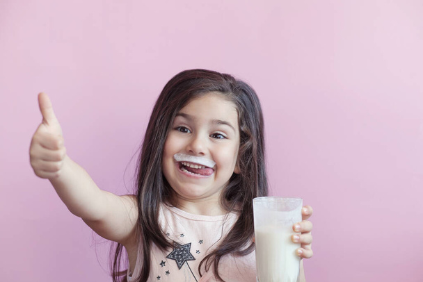 Маленькая улыбающаяся девочка пьет молоко из стакана - Фото, изображение