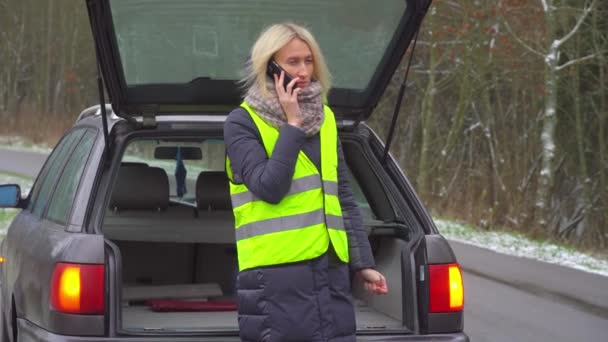 Egy nő telefonál az okostelefonján, miközben egy lerobbant autó mellett áll.. - Felvétel, videó