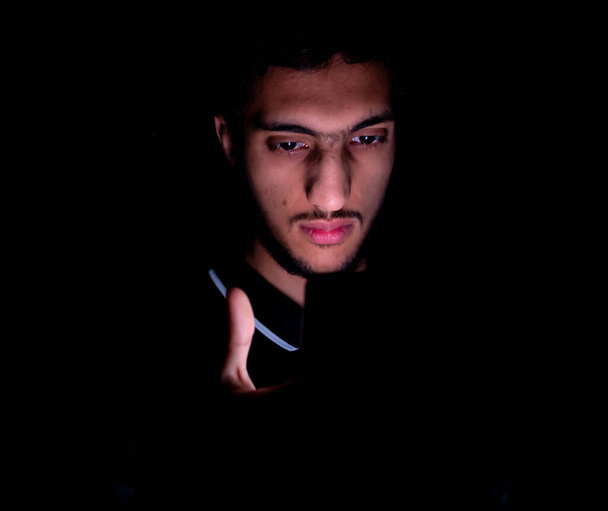 Portrét chlápka z Blízkého východu, jak kontroluje telefon v tmavé místnosti - Fotografie, Obrázek