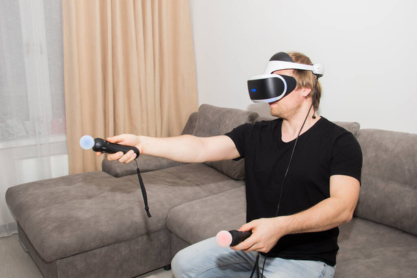 Une personne joue dans la réalité virtuelle. Un jeune homme joue à un jeu d'ordinateur dans des lunettes blanches d'un casque de réalité virtuelle. - Photo, image