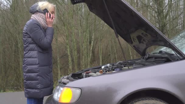 Eine Frau ruft auf ihrem Smartphone an, während sie am kaputten Auto steht. - Filmmaterial, Video