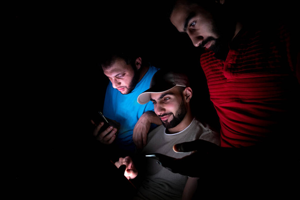 портрет ближневосточных парней, сидящих вместе в темной комнате - Фото, изображение