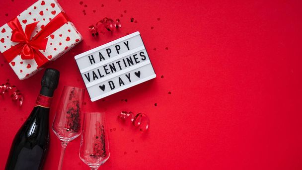 Valentines day banner concept.Board with text happy valentines day,gift box with bow,serpentine,champagne,glasses and heart shaped confetti on red background, top view, flat lay, copy space - Photo, Image