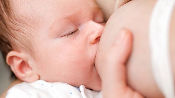 Closeup portrait of cute 1 month old newborn baby sucking mothers breast while eating milk. Concept of healthy and natural baby breastfeeding nutrition. - 写真・画像