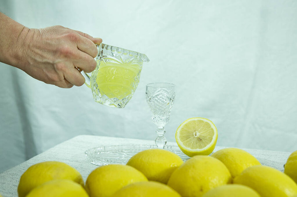 Limoncello. Mano femenina vertiendo una bebida en un vaso. Licor de limón casero tradicional limoncello y cítricos frescos en un plato blanco, enfoque selectivo. - Foto, imagen