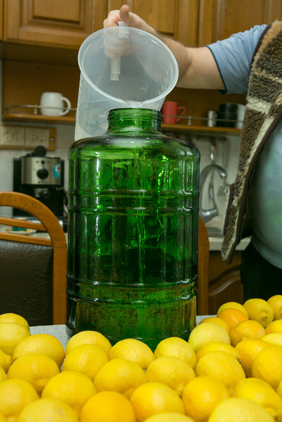 Le processus de fabrication de la liqueur de citron limoncello à la maison. L'homme verse de l'alcool dans un grand récipient. - Photo, image