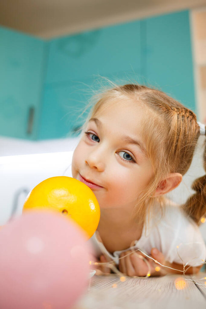 Una niña de siete años lleva una camiseta blanca. Juega con mandarinas maduras - Foto, Imagen