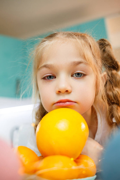 Una ragazza di sette anni indossa una maglietta bianca. Gioca con mandarini maturi - Foto, immagini