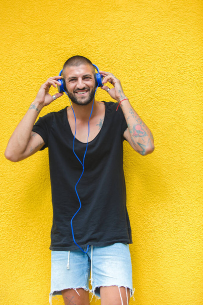 Татуювання чоловік слухає музику за допомогою навушників на жовтій стіні
 - Фото, зображення